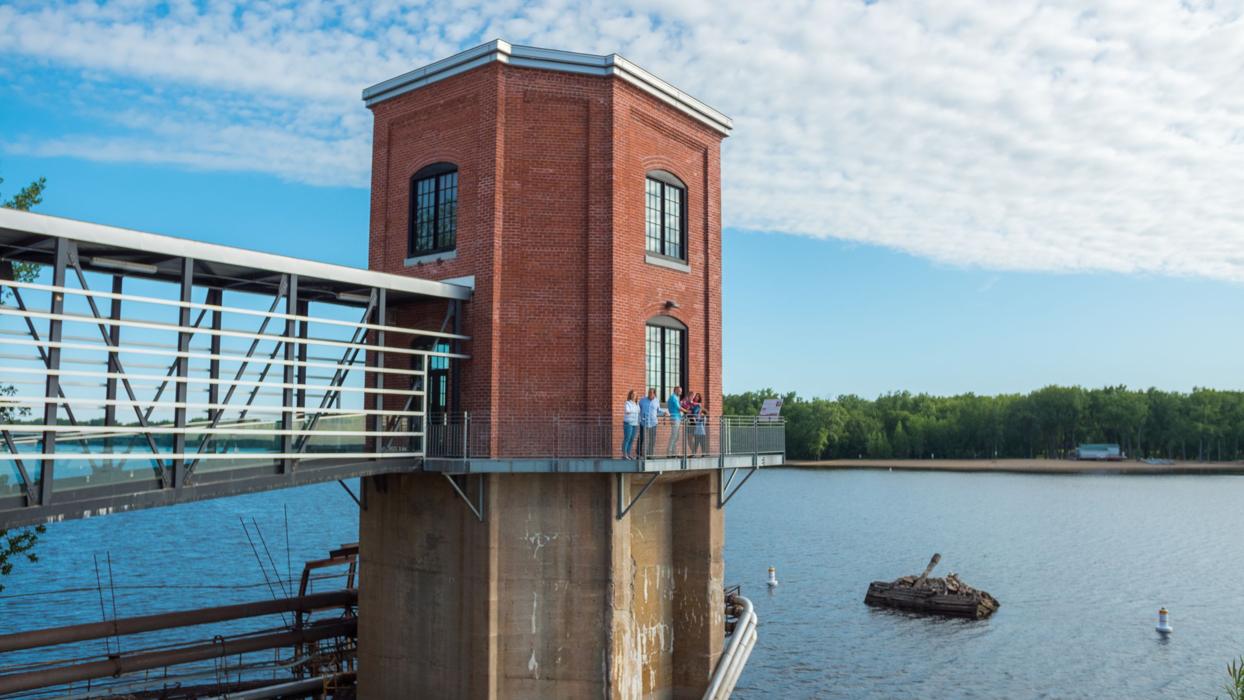 Des visiteurs observent le paysage depuis la tour du musée Boréalis, en brique rouge et perchée au-dessus de la rivière, accessible par une passerelle vitrée.
