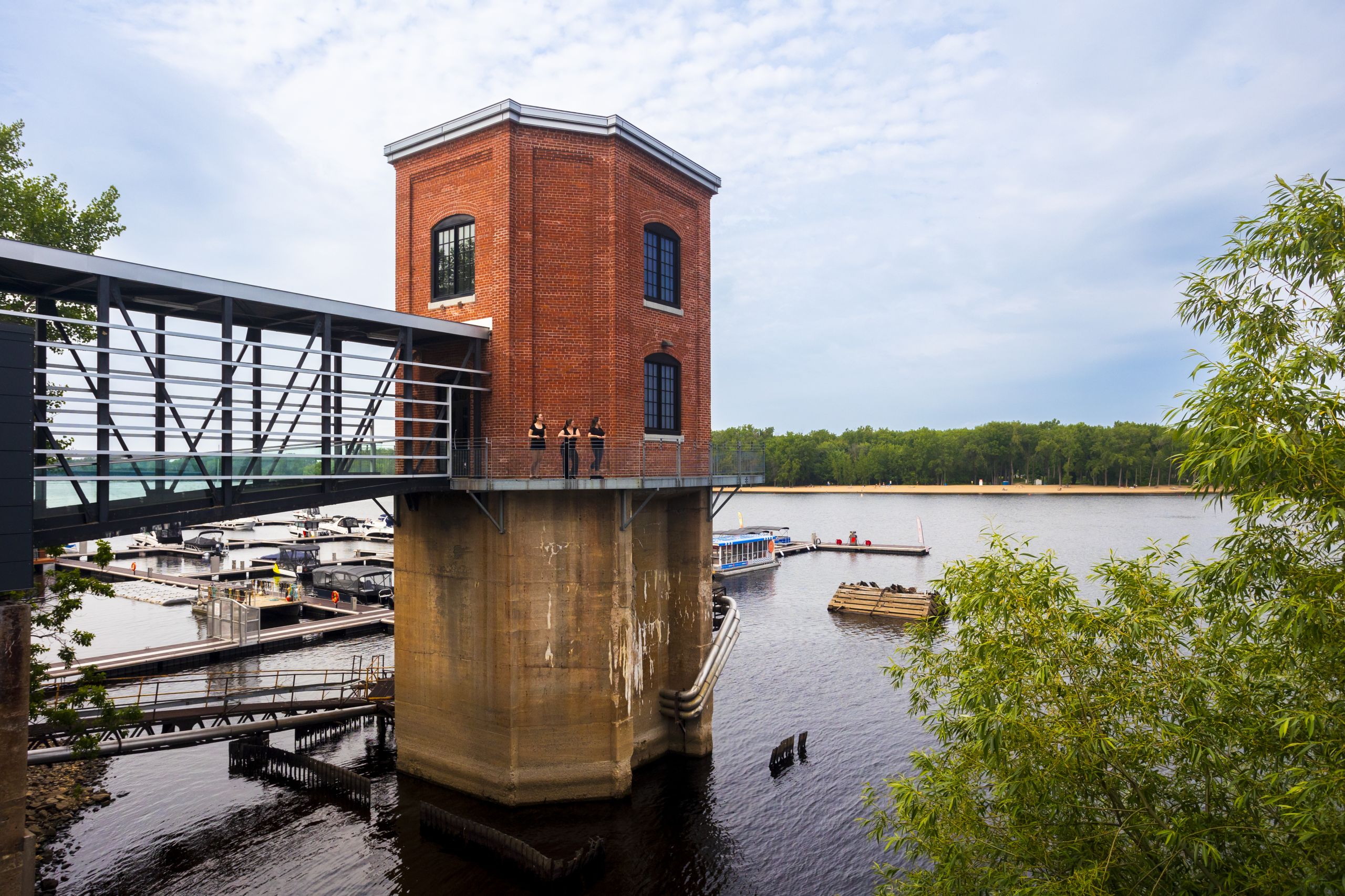 Des visiteurs observent le paysage depuis la tour du musée Boréalis, en brique rouge et perchée au-dessus de la rivière, accessible par une passerelle vitrée.